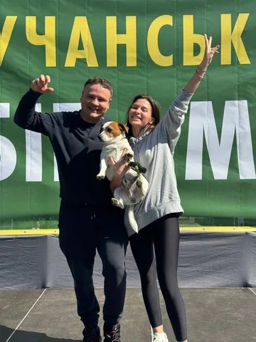 Двоє людей з собакою піднімають руки на спортивному заході