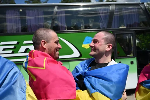 Двоє чоловіків у національних прапорах обіймаються біля автобуса