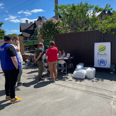 Люди біля пункту видачі допомоги з логотипом UNHCR