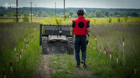 Сапер у червоній жилетці біля робочої машини на мінованому полі