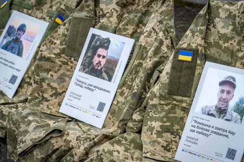 Портрети військовослужбовців на камуфльованому матеріалі з українськими прапорцями