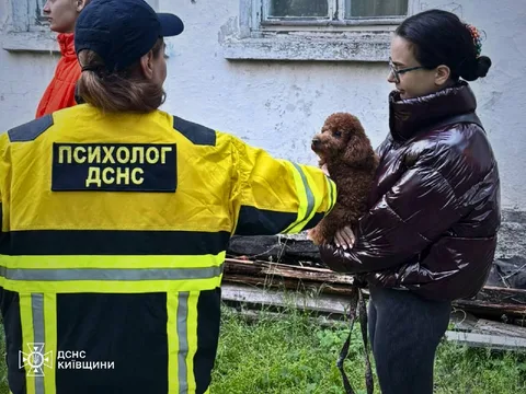 Психолог у жовтому жилеті спілкується з жінкою біля пошкодженої будівлі