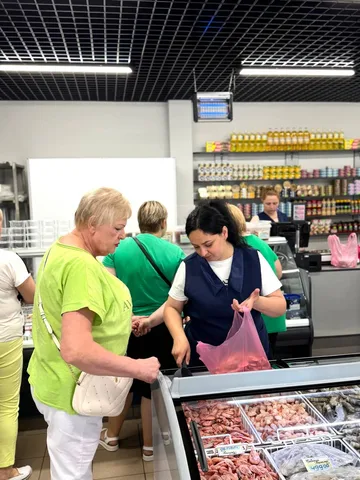 Покупиця в жовтій футболці розмовляє з продавцем у м'ясному відділі магазину