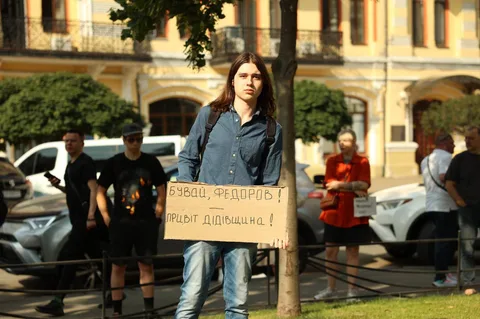 Жінка з плакатом на площі біля будівлі, люди навколо